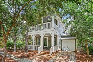 A two-story house with a porch, a garage, and bicycles parked outside. - The Greenhouse (Santa Rosa Beach)
