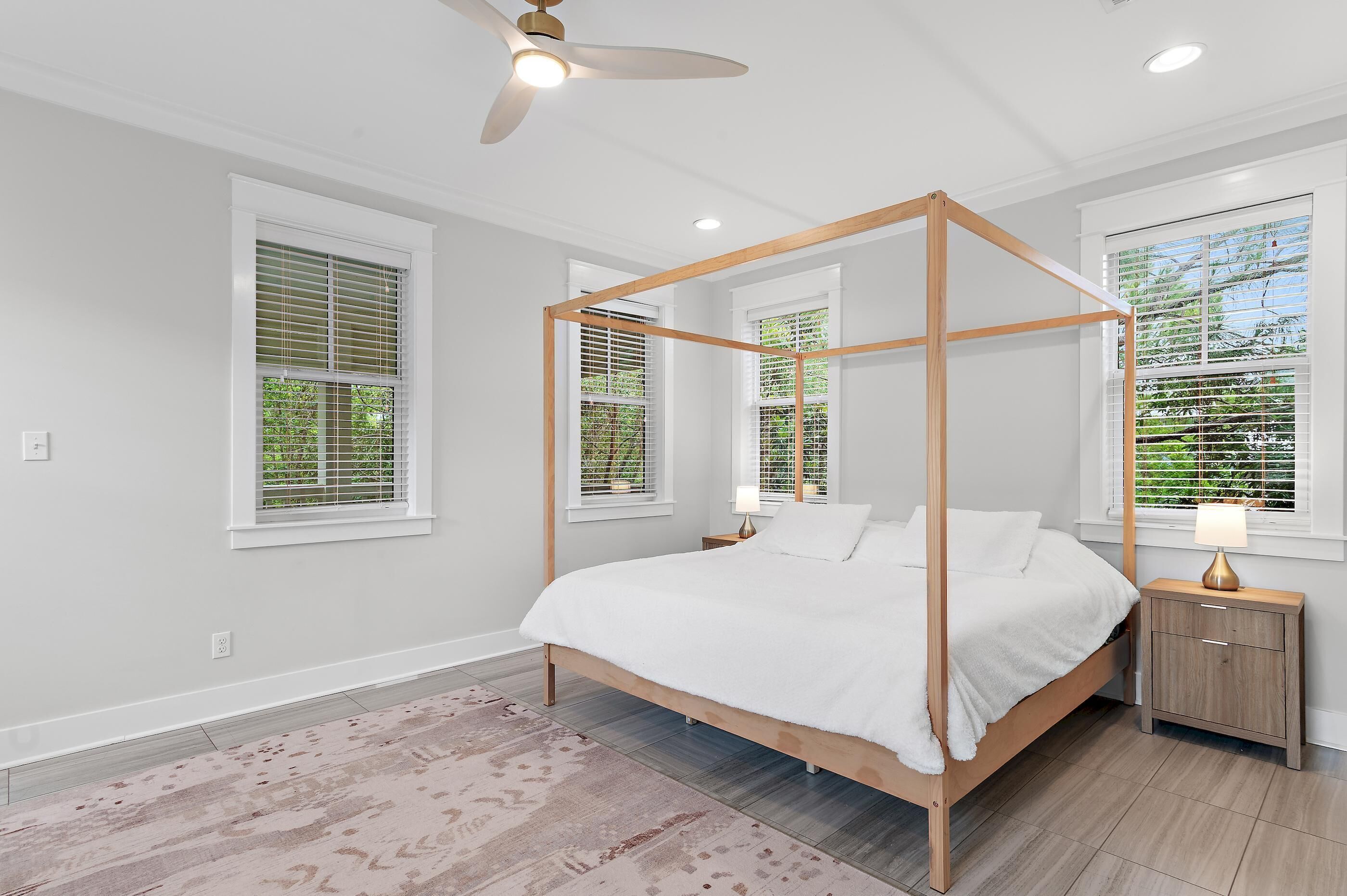 A four-poster bed with a wooden frame, a bedside table with a lamp, and a ceiling fan.