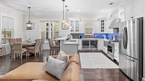 A spacious kitchen with white cabinetry, a stainless steel refrigerator, and a dining area with wicker chairs and a brown sofa. - Jaybird Bungalow (Santa Rosa Beach)