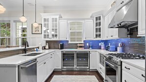 A modern kitchen with white cabinetry, a stainless steel stove, and a blue-tiled backsplash. - Jaybird Bungalow (Santa Rosa Beach)