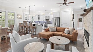 A modern kitchen with white cabinets, stainless steel appliances, and a dining area with wicker furniture. - Jaybird Bungalow (Santa Rosa Beach)