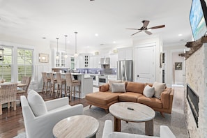 A modern kitchen with white cabinets, stainless steel appliances, and a dining area with wicker furniture. - Jaybird Bungalow (Santa Rosa Beach)