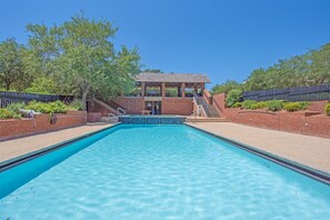 A rectangular swimming pool with a brick structure in the background, surrounded by a fence and trees. - Jaybird Bungalow (Santa Rosa Beach)