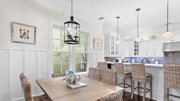 A modern kitchen with white cabinetry, a wooden dining table, wicker chairs, pendant lights, and a view of the outdoors. - Jaybird Bungalow (Santa Rosa Beach)