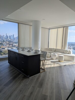 A modern living room with a large window, a white sofa, and a dark wooden cabinet. - Beautiful luxury high-rise condo with views of downtown Los Angeles in Koreatown (Vernon)