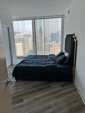 A bedroom with a bed, a window with blinds, and a view of buildings. - Beautiful luxury high-rise condo with views of downtown Los Angeles in Koreatown (Vernon)