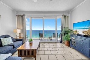 Ein Wohnzimmer mit einer Couch, Couchtisch, Fernseher und einem Balkon mit Meerblick.