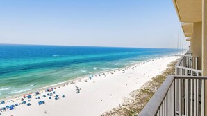 Blick auf einen Strand vom Balkon aus, mit blauem Himmel, Sandstrand und ruhiger See.