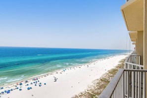 Blick auf einen Strand vom Balkon aus, mit blauem Himmel, Sandstrand und ruhiger See.