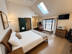 A bedroom with a bed, a TV, a microwave, a chair, a window, and a door.