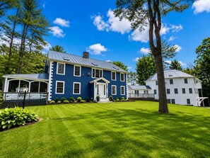 A large, two-story house with a blue exterior, a front porch, and a well-maintained lawn.