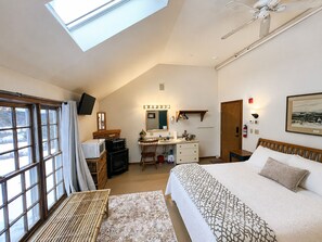 Une chambre à coucher comprenant un lit, un bureau, une chaise, un téléviseur et une fenêtre de toit.