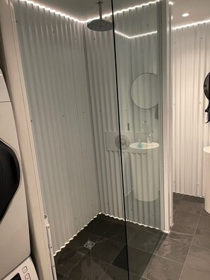 Un baño moderno con cabina de ducha de vidrio, un espejo redondo y un lavabo.