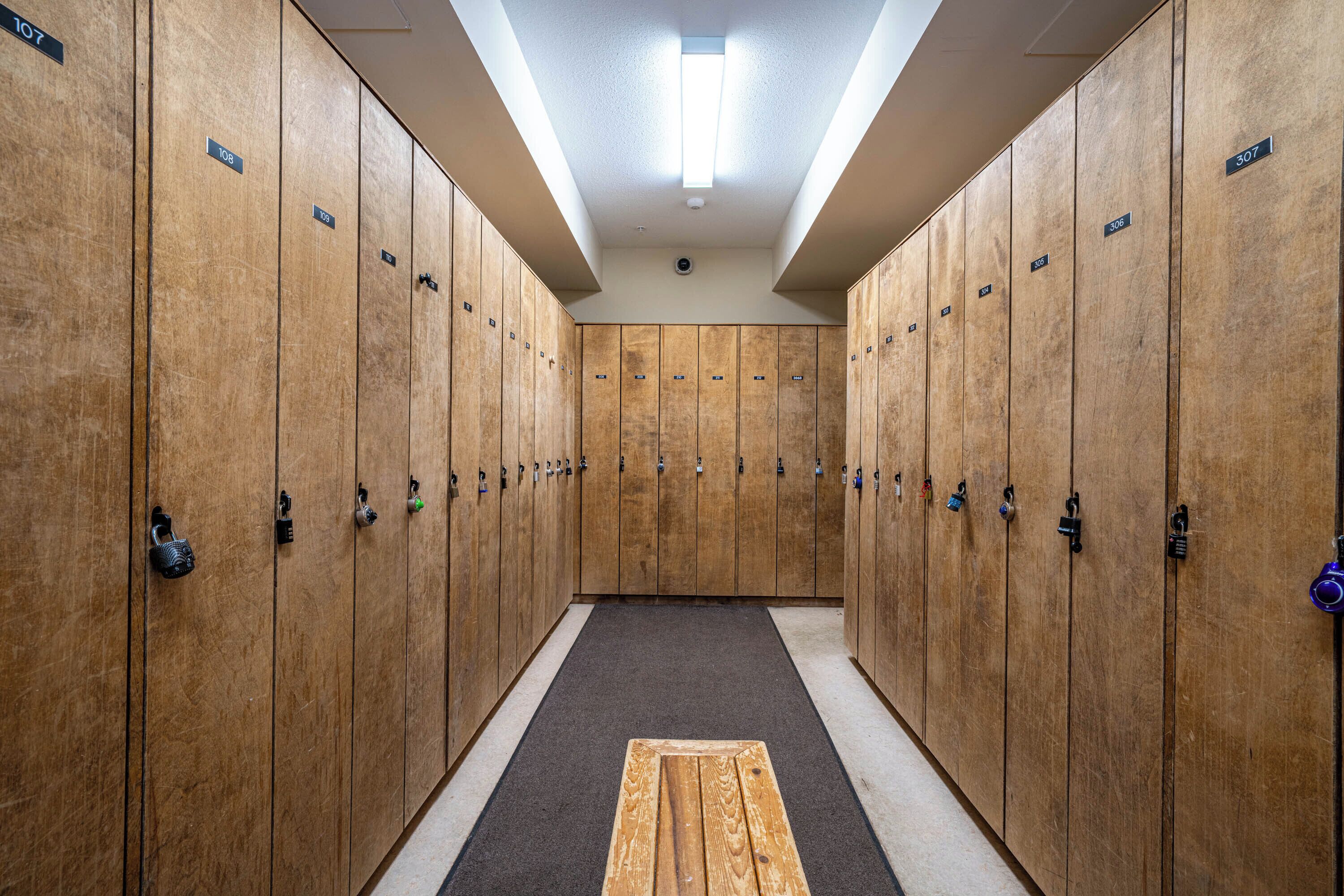 A row of wooden lockers with numbered tags, a central wooden bench, and a ceiling light.