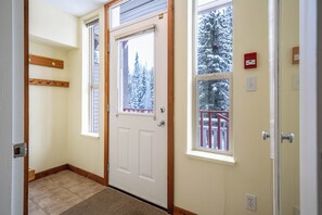 Ein Flur mit einer weißen Tür, einem Fenster mit Blick auf schneebedeckte Bäume und einem roten Rauchmelder an der Wand.
