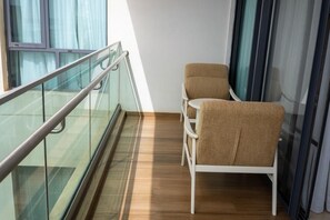Uma varanda com guarda-corpo de vidro, duas cadeiras e piso de madeira.