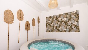Ett spa-rum med ett bubbelbad, trädekorationer formade som löv som sitter på väggen och ett väggkonstverk med ett blommönster.
