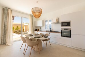 A modern kitchen with white cabinets, a dining table set for four, and a large window with curtains. - Villa Harem - Santa Maria Del Fo... (Santa maria del focallo)