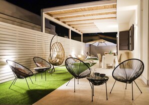 Un patio al aire libre con sillas modernas, una silla colgante y una zona de comedor con mesa y sillas.