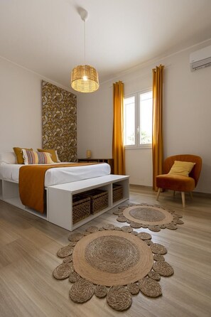 Un dormitorio moderno con cama, mesita de noche, silla, lámpara colgante y ventana con cortinas.