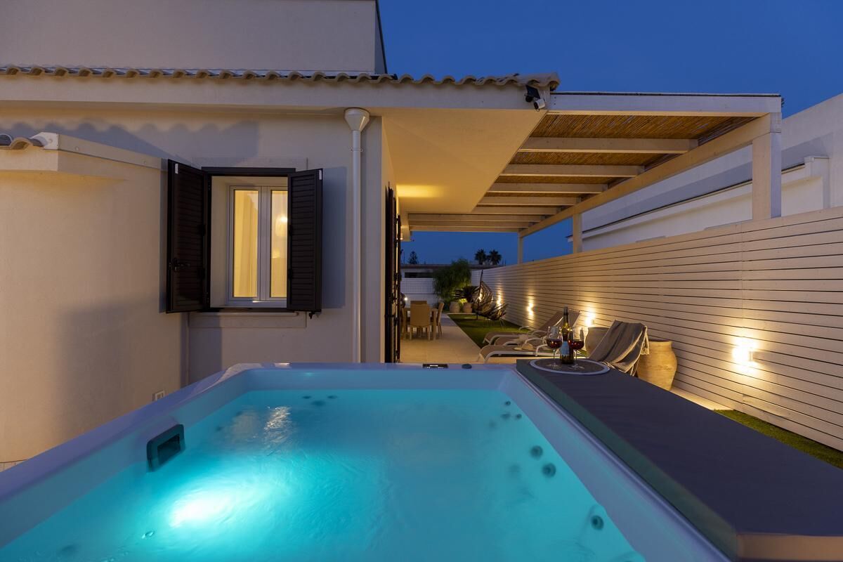 A hot tub with a wooden deck and lounge chairs, a covered patio area, and a view of the backyard.