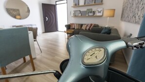 Una stanza con uno scooter azzurrognolo, un tavolo da pranzo con sedie, un divano, una lampada e una parete con quadri appesi.