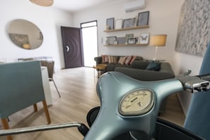 Una habitació amb un patinet blau clar, una taula de menjador amb cadires, un sofà, una làmpada i una paret amb quadres.