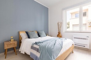 Ein Schlafzimmer mit Bett, Nachttisch, Lampe, Fenster und Klimaanlage.