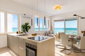 Eine moderne Küche mit einer großen Kochinsel, ein Essbereich mit Meerblick und ein Balkon mit gedecktem Tisch.