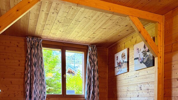 En stuga med träpanel, ett rum med en säng, två fönster med gardiner och konst på väggarna.
