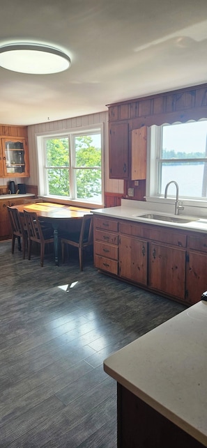 A kitchen with wooden cabinets, a dining table, and a large window overlooking a body of water. - 3-bedroom cottage on Forest Lake in Windham (Windham)