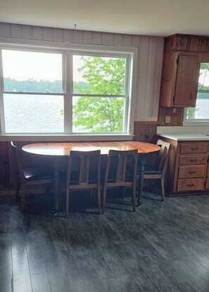 A kitchen with a large window, wooden cabinets, and a dining table with chairs. - 3-bedroom cottage on Forest Lake in Windham (Windham)