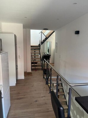 Une cuisine moderne dotée d’un réfrigérateur, d’un plancher en bois, d’un escalier avec une rampe en métal et d’un mur de couleur claire.