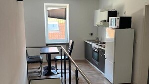 Kompakti keittiö, jossa on jääkaappi, mikroaaltouuni ja liesi. Keittiössä on ruokailutila, jossa on pöytä ja tuolit, sekä ikkuna, josta tulee luonnonvaloa.