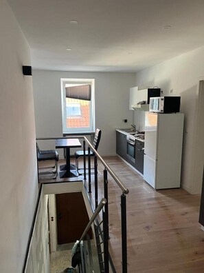 A compact kitchen with a refrigerator, microwave, and stove. There is a dining area with a table and chairs, and a window providing natural light. - Kaiserslautern Entire Building  · 8 Rooms · Sleeps 13 · 3 Private Kitchens · KMC (Kaiserslautern)