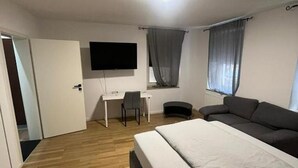 Makuuhuoneessa on sänky, työpöytä, tuoli, televisio ja ikkuna, jossa on verhot.
