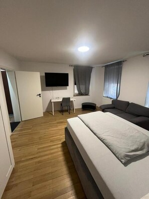 Ett sovrum med en säng, ett skrivbord, en stol, en tv och ett fönster med gardiner.