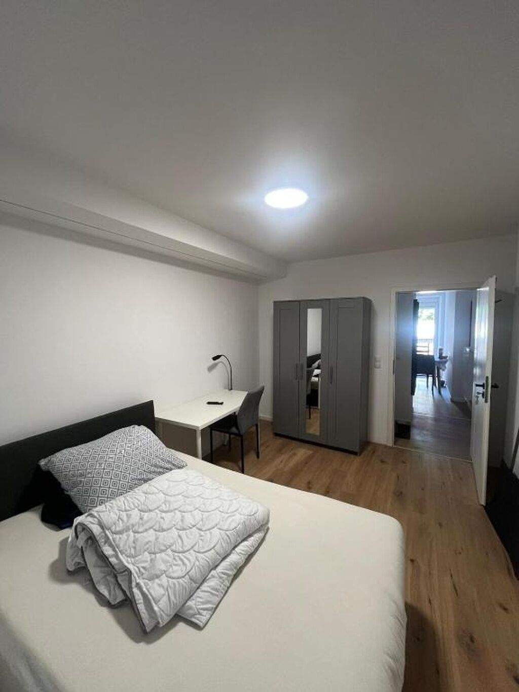 A bedroom with a bed, a desk, and a wardrobe.