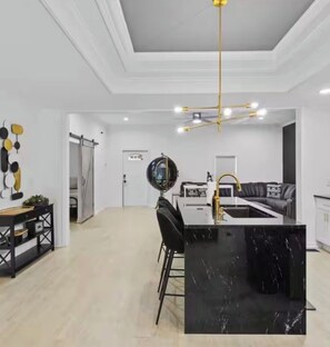 A modern kitchen with a black marble island, a black and white sofa, and a ceiling light fixture. - Spacious Home - Near Duke Hospital, Downtown Durham & RTP (Durham)