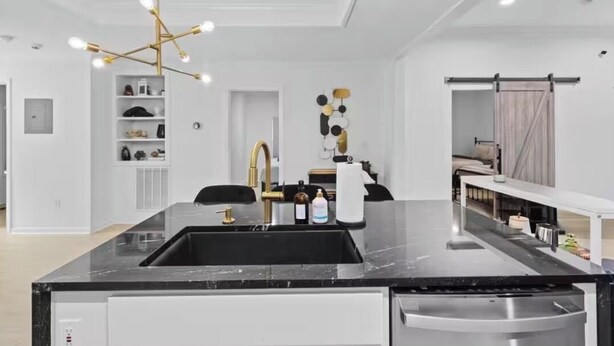 Een moderne keuken met een zwart marmeren aanrechtblad, roestvrijstalen apparatuur en een gouden hanglamp.