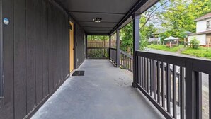 Een overdekte veranda met een metalen hekwerk, een deur aan de linkerkant en uitzicht op een woonstraat.