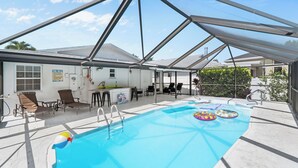 A covered swimming pool with lounge chairs, a bar area, and a 'POOL RULES' sign. - Coastal Naples Escape Private Pool, Sleeps 12, Vanderbilt Beach 5 mins away (Naples)