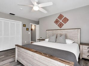 A bedroom with a bed, a nightstand, a ceiling fan, a wardrobe, and decorative wall art. - Coastal Naples Escape Private Pool, Sleeps 12, Vanderbilt Beach 5 mins away (Naples)