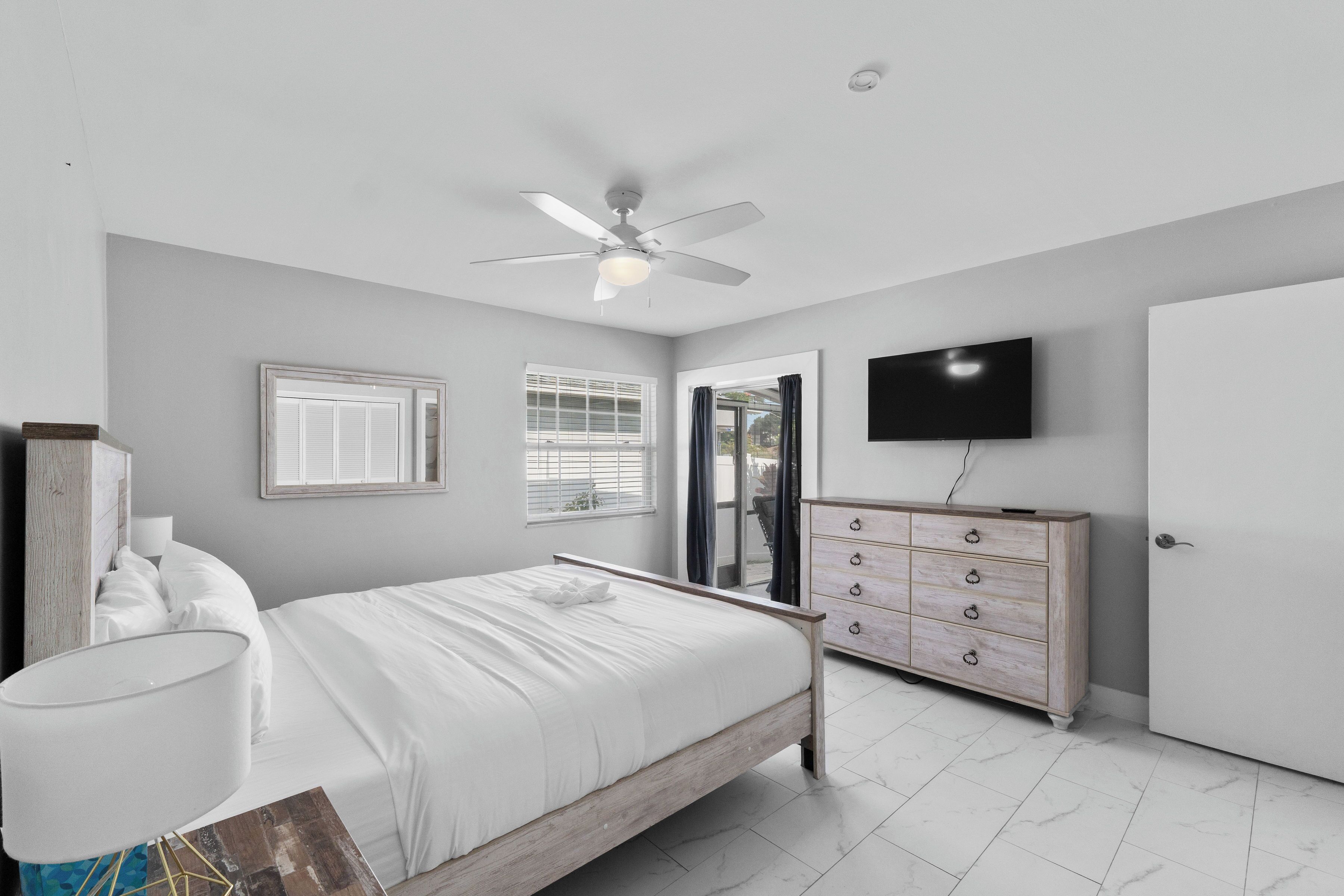 Un dormitorio con cama, ventilador de techo, cómoda, televisor y una puerta.