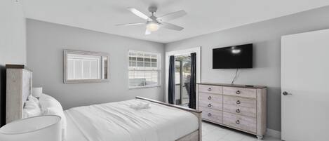 Un dormitorio con cama, ventilador de techo, cómoda, televisor y una puerta.
