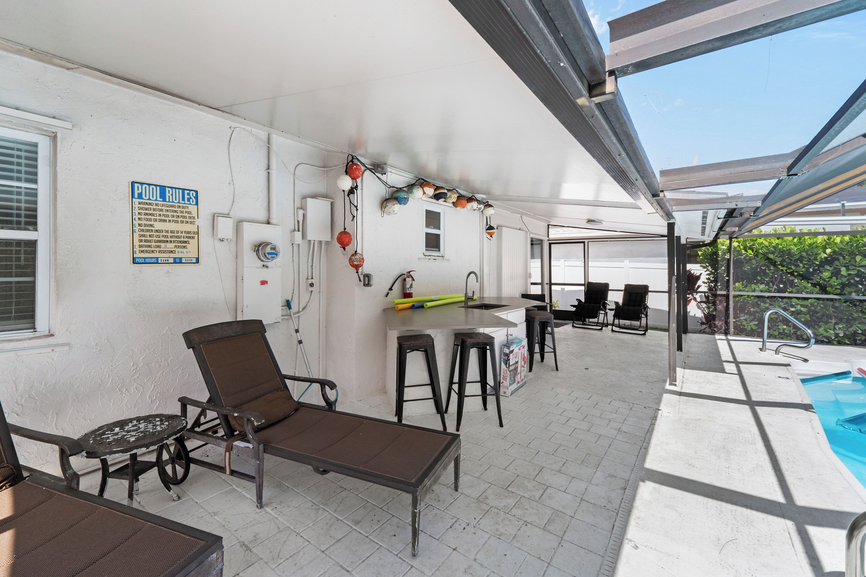 Un espace extérieur abrité comprenant une piscine, un bar, des chaises longues et un panneau indiquant les règles d’utilisation de la piscine.