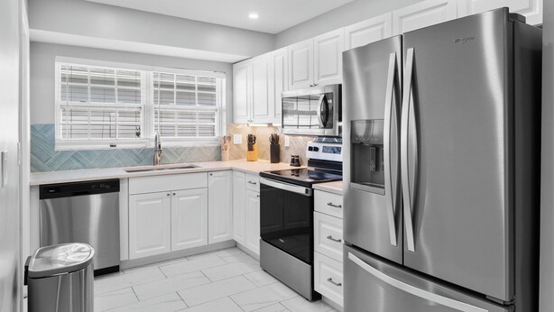 A modern kitchen with stainless steel appliances, white cabinetry, and a window with blinds. - Coastal Naples Escape Private Pool, Sleeps 12, Vanderbilt Beach 5 mins away (Naples)