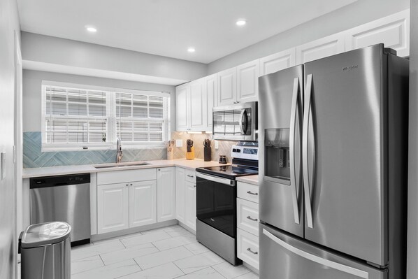 A modern kitchen with stainless steel appliances, white cabinetry, and a window with blinds.