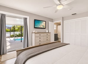 Un dormitorio con cama, cómoda, ventilador de techo, televisor y vista a una piscina.