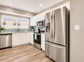 Una cocina moderna con electrodomésticos de acero inoxidable, armarios blancos y piso de madera.